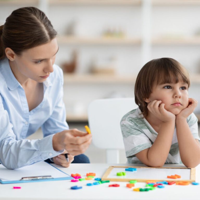 Bored sad little boy refusing to cooperate with his private teacher, ignoring speech therapist with colorful letters at office, free space