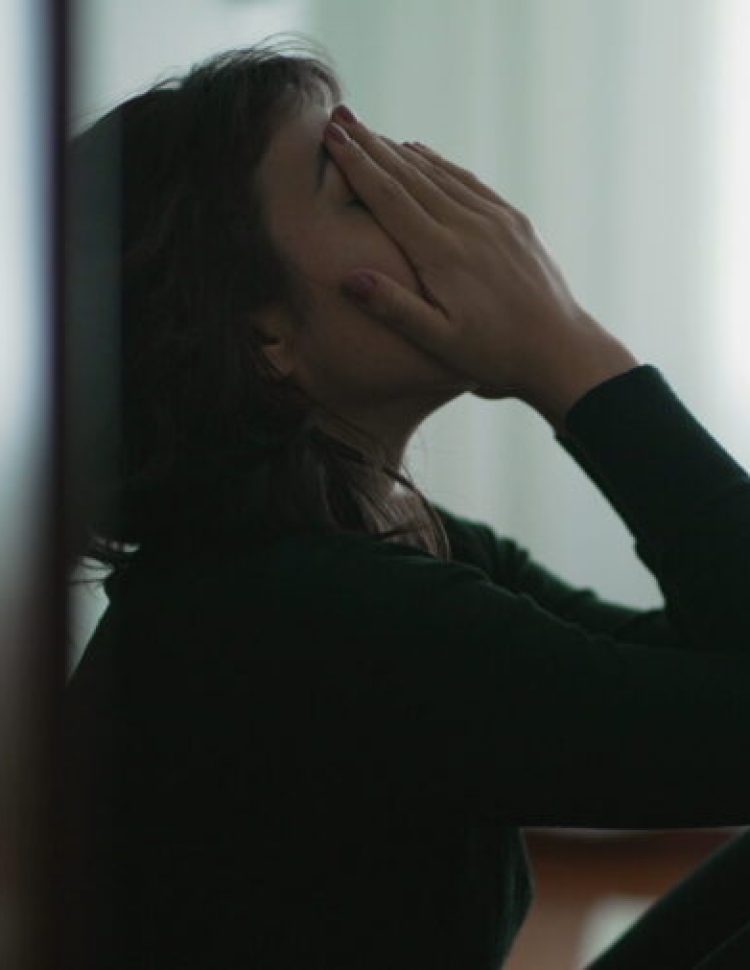 Depressed woman sitting on floor covering face with hands in despair