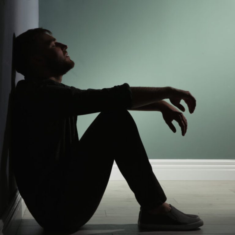 Depressed young man sitting on floor in darkness
