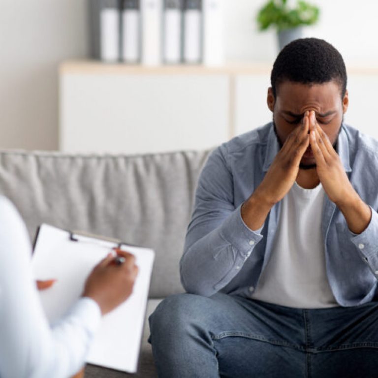 Desperate black man suffering from nevrous breakdown or depression, having session at psychologist's office, panorama. Stressed male patient meeting with therapist, receiving professional assistance