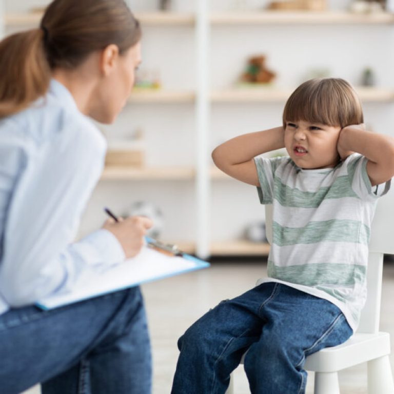 Professional psychotherapist trying to talk to difficult kid, grumpy little boy covering ears and frowning nose, ignoring psychologist during session
