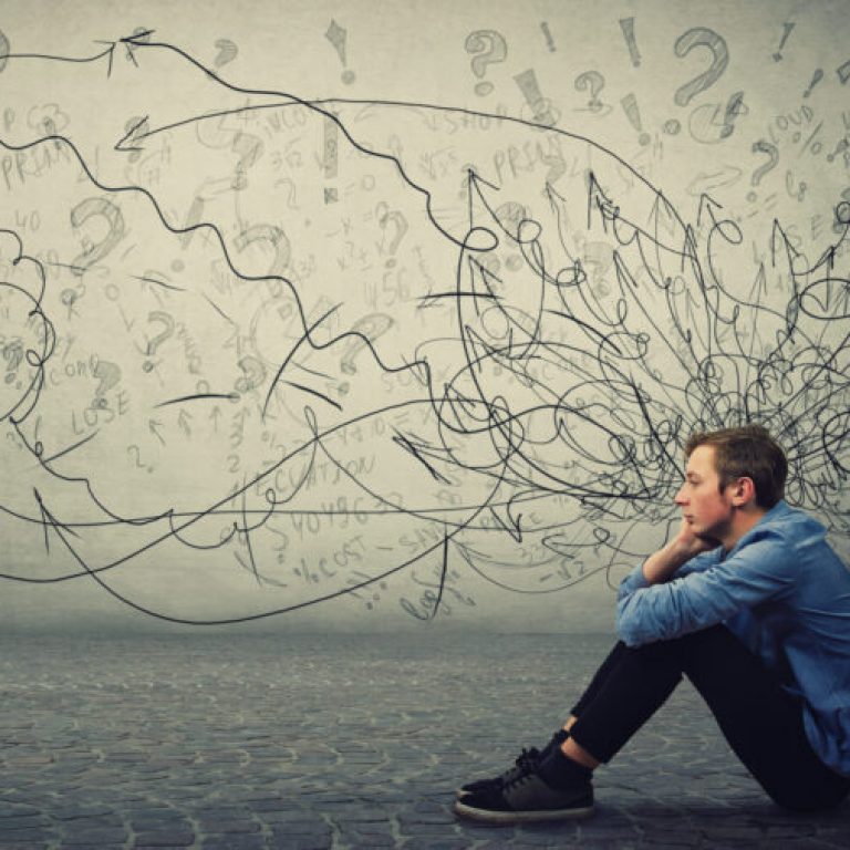 Upset and tired boy teenager sitting on the floor keeps hand to cheek looking thoughtfully and hopeless. Stressed student guy feels emotional discomfort, anxiety and mental health problems.